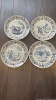 Four Boch Belgium Delft blue plates arranged together on floor showing different scenic Dutch village and countryside designs.