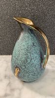 Front and side view of JASBA turquoise and gold vase showing matte textured glaze with gold accents and smooth curved handle.
