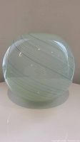 Side view of spherical Murano glass vase with light green and aqua swirl pattern covered in clear glossy glass.