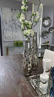 Two tall hammered silver vases on a wooden table with decorative branches inside one