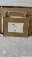 Framed lithograph in gold-tone frame with beige mat, showing minimalist stylized goose artwork.