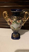 Front view of vintage Chinese bud vase showing floral hand-painted design, blue and gold colors, and two gold handles.