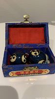 Open blue fabric box showing two blue Baoding balls with yin-yang and circular symbols inside with red lining