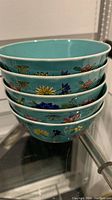 Five stacked turquoise soup bowls with colorful floral hand-painted designs.