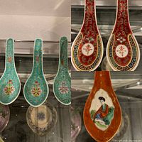 Six vintage Chinese soup spoons showing various decorative styles including turquoise cloisonné floral designs, red spoons with Chinese characters, and spoon with painted woman figure.