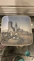 Front view of square ceramic plate with cityscape and storks artwork