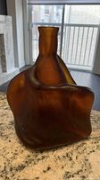 Front side view of the abstract shaped mid-century brown and amber glass vase on a granite surface near window.