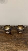 Two-piece silver plated cream and sugar set on wooden surface showing front view.