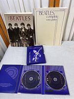 Photo of three main items: The Beatles: Unseen Archives book, Beatles Complete Easy Guitar sheet music book, and Concert for George DVD sleeve with two discs inside.