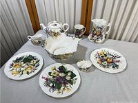 Collection of bone china floral dishware showing teapot, creamer, pitcher, large bowl, plates, and mug arranged on a white surface against a neutral background.