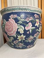 Front view close-up of ceramic planter showing pink, yellow, orange flowers on deep blue background with white rim and green leaf garland detail.