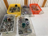 Top view of five different plastic containers filled with assorted shot glasses of various sizes and designs.