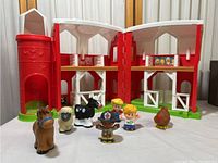 Photo of open Fisher Price farmhouse barn with six farm-themed figurines positioned inside and in front of barn, showing the playset's scaled size and design