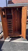 Armoire doors open showing interior cedar lining, six drawers on left, hanging rod and hat hooks on right