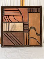 Full view of the square wooden mosaic showing geometric and curved wood pieces of varying shades inside a dark frame.