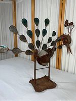 Front side view of metal peacock sculpture showing painted and patina-style metal feathers and rusted body and base.