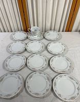 Top-down photo of eleven small Noritake Ireland china plates and one cup with saucer arranged on table.