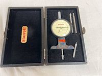 Open black case containing Starrett dial indicator, two metal rods and a small metal attachment, case lid displaying Starrett logo.