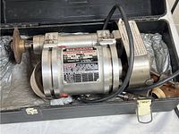 Themac precision grinder inside black carrying case with foam padding and broken latch visible.