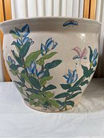 Front view of ceramic planter showing hand-painted blue flowers and green leaves, with a small blue butterfly detail near the rim.