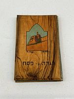 Front cover of antique Haggadah book with olive wood painted depiction of a fortress and Hebrew text.
