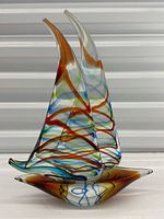 Clear front view of the art glass sailboat sculpture showing two tall sails with multicolored swirls and brown base.