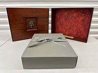 Grey linen slipcover open to reveal mahogany cabinet with bronze relief on front and red marbled interior