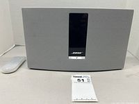 Front view of Bose SoundTouch 20 wireless speaker in grey with black control panel and white remote control laying beside it.