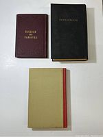 Photo showing all three books: Hagadah for Passover (maroon cover), Pentateuch (black cover), and a third book with beige and red cover.