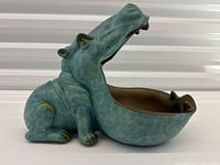 Side view of the blue-green hippopotamus shaped bowl with open mouth forming the bowl interior showing brown color inside and gold accents on feet and eyes.