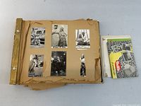 Opened scrapbook showing multiple mounted black-and-white photos and loose envelope pack at right