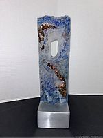 Front view of signed blue and clear textured art glass sculpture with copper accents on silver aluminum base