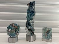 Three sculptures displayed side by side on aluminum bases