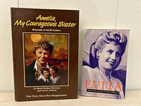 Two books placed side by side: 'Amelia, My Courageous Sister' hardcover and 'Evita: The Real Lives of Eva Peron' paperback.