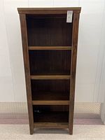 Front view of tall wooden bookshelf with four shelves and wood panel back