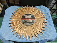 Full top down view of large 38 inch diameter starburst wall mirror on blue blanket. Central beveled mirror is visible but detached from wood frame around perimeter.