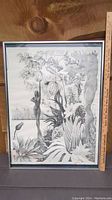 Framed black and white print showing the artwork with detailed nude figures, plants, and a tiger with a wooden ruler for size reference.