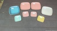 Set of eight Glidden pottery plates arranged on a table, showing four larger 7-inch plates and four smaller 4-inch plates in various pastel colors with original dealer price stickers.