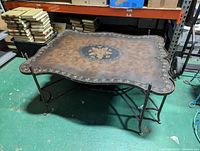 Photo of the coffee table from an angled side view showing the leather top and carved iron base.