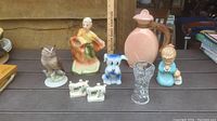 Front view of lot with all items arranged on a wooden surface: red wing water pitcher, owl figurine, person valet holder, dog coin bank, mother and baby figurine, sewing machine S&P set, crystal vase.