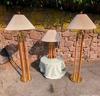 Three lamps: two floor and one table, arranged outdoors against stone wall