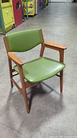 Front angled view of the mid-century armchair showing green leather seat and walnut frame.