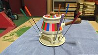Retro 1970s fondue pot set on stand with six colorful fondue forks arranged around it, placed on a blue cloth.