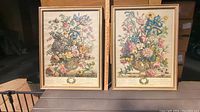 Two large botanical prints side by side on a table, framed with faux bamboo glass frames, depicting colorful floral bouquets titled Spring and Summer.