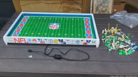 Overall view of the Tudor NFL Electric Football board with many player pieces grouped on the right side, showing the full field, electric cord with switch, and NFL logos around the perimeter.