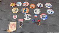 Full lot of 18 pinback buttons, small notebook and H. Humphrey figurine on dark wooden table showing variety of political and other themes