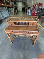 Front view of the vintage rattan bamboo writing desk showing the base, pull-out surface, and upper shelf with drawers.