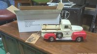 Vintage style red and cream pickup truck on a wooden table next to its opened box and tags.
