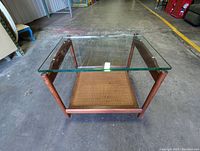 Top-down view showing clear thick glass resting perfectly within the solid teak frame with tightly woven caned shelf below.