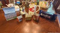 Seven pieces of vintage WADE porcelain displayed on a wooden table including four miniature houses, a Milky Way bank, Nova Scotia mug, and floral creamer.